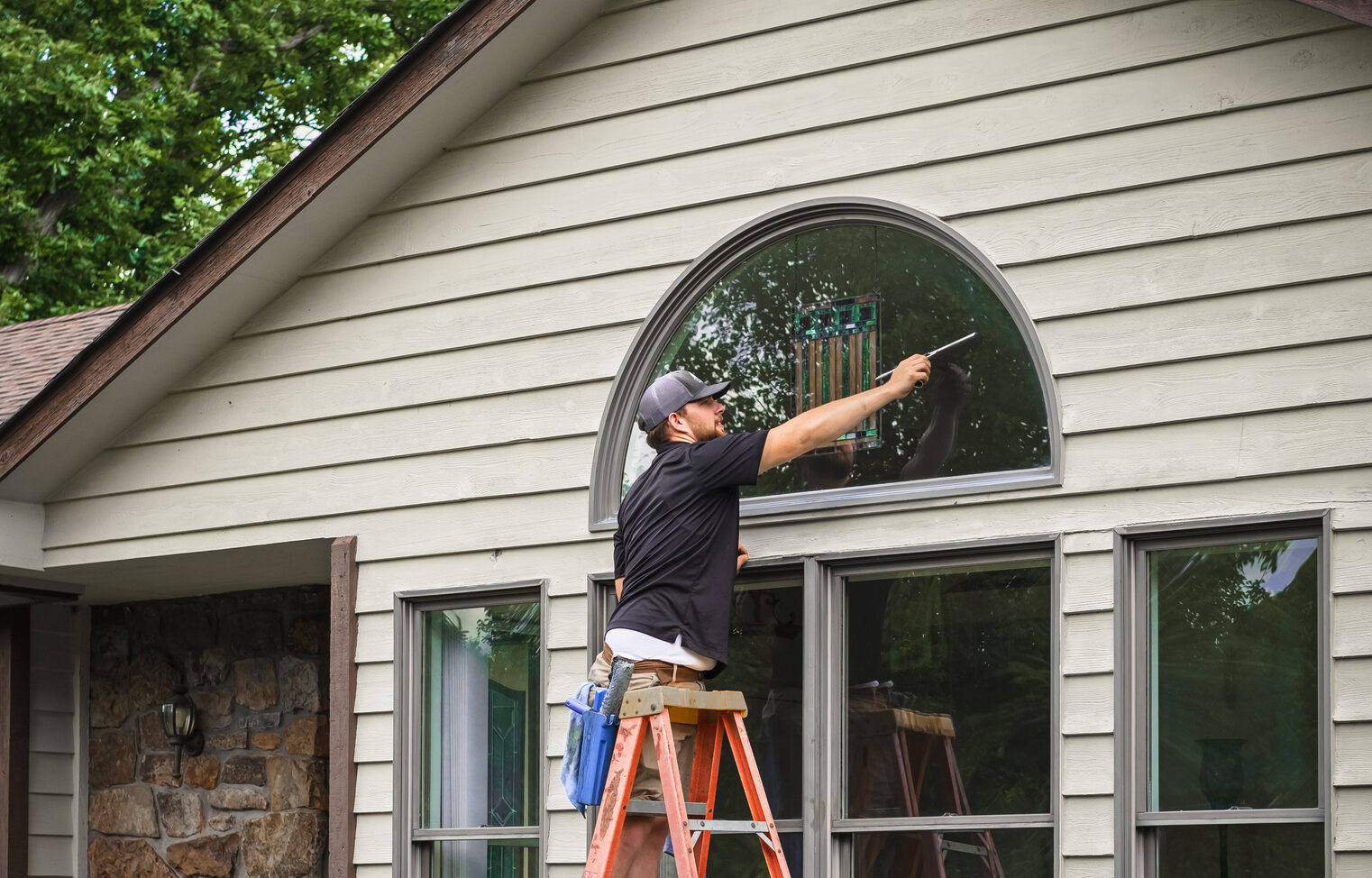 Young man standing on ladder washing outside windows of Midwestern house Young man standing on ladder washing outside windows of Midwestern house